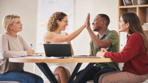 Équipe de quatre jeunes collègues souriants se tapant dans la main autour d'une table de réunion avec ordinateur portable