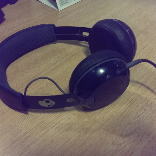 Casque audio Skullcandy noir posé sur un bureau en bois, avec son câble.