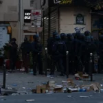 Rue de Paris jonchée de cartons et de débris devant des commerces fermés, avec des policiers en tenue anti-émeute, le 17 octobre 2026