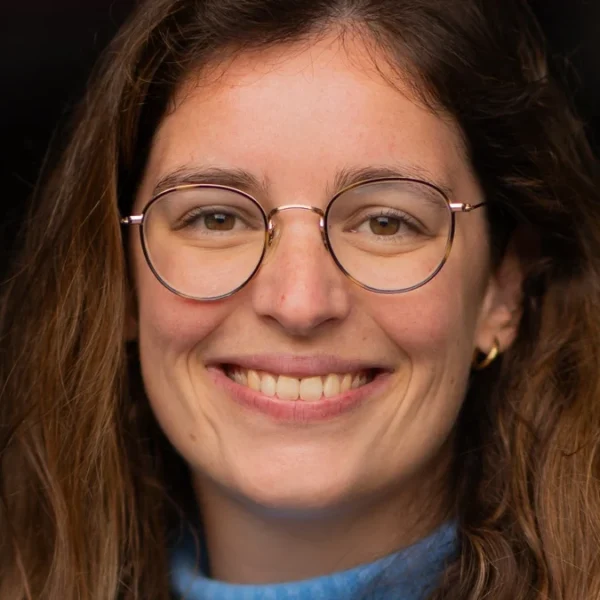 Portrait de Clotilde Mérillon, souriante, avec des lunettes et un pull bleu.