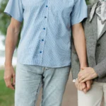 Un homme en chemise bleue et une femme en veste grise se tiennent la main dans un parc.