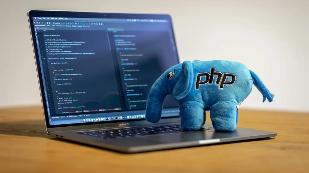Un éléphant bleu en peluche portant le logo PHP posé sur un ordinateur affichant du code.