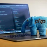 Un éléphant bleu en peluche portant le logo PHP posé sur un ordinateur affichant du code.