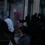 Vitrine brisée et taguée d’un commerce à Paris, avec plusieurs personnes devant, le 17 octobre 2026.