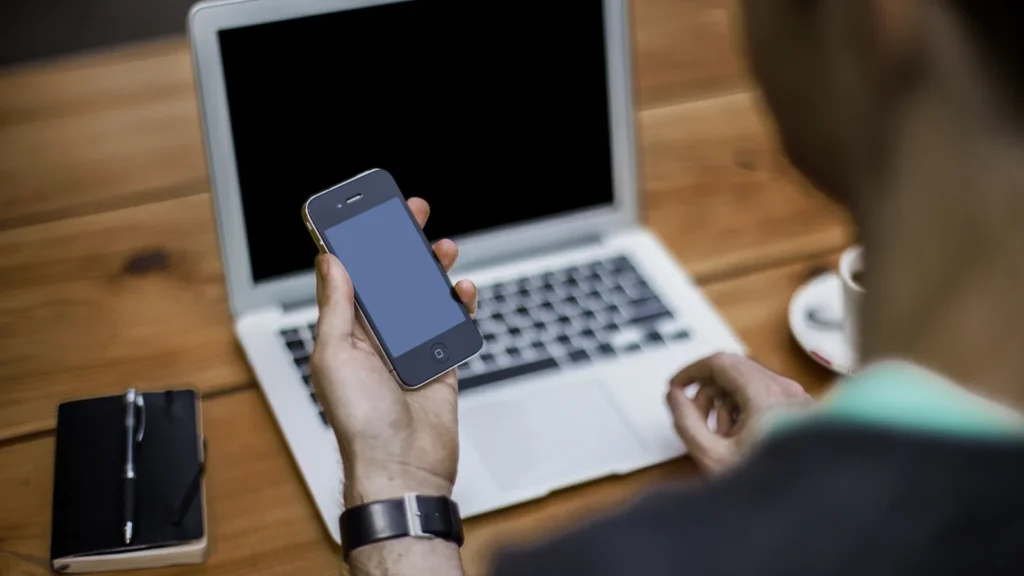 Homme utilisant un ordinateur portable et un smartphone à un bureau, photo d’illustration de l’apprentissage numérique.
