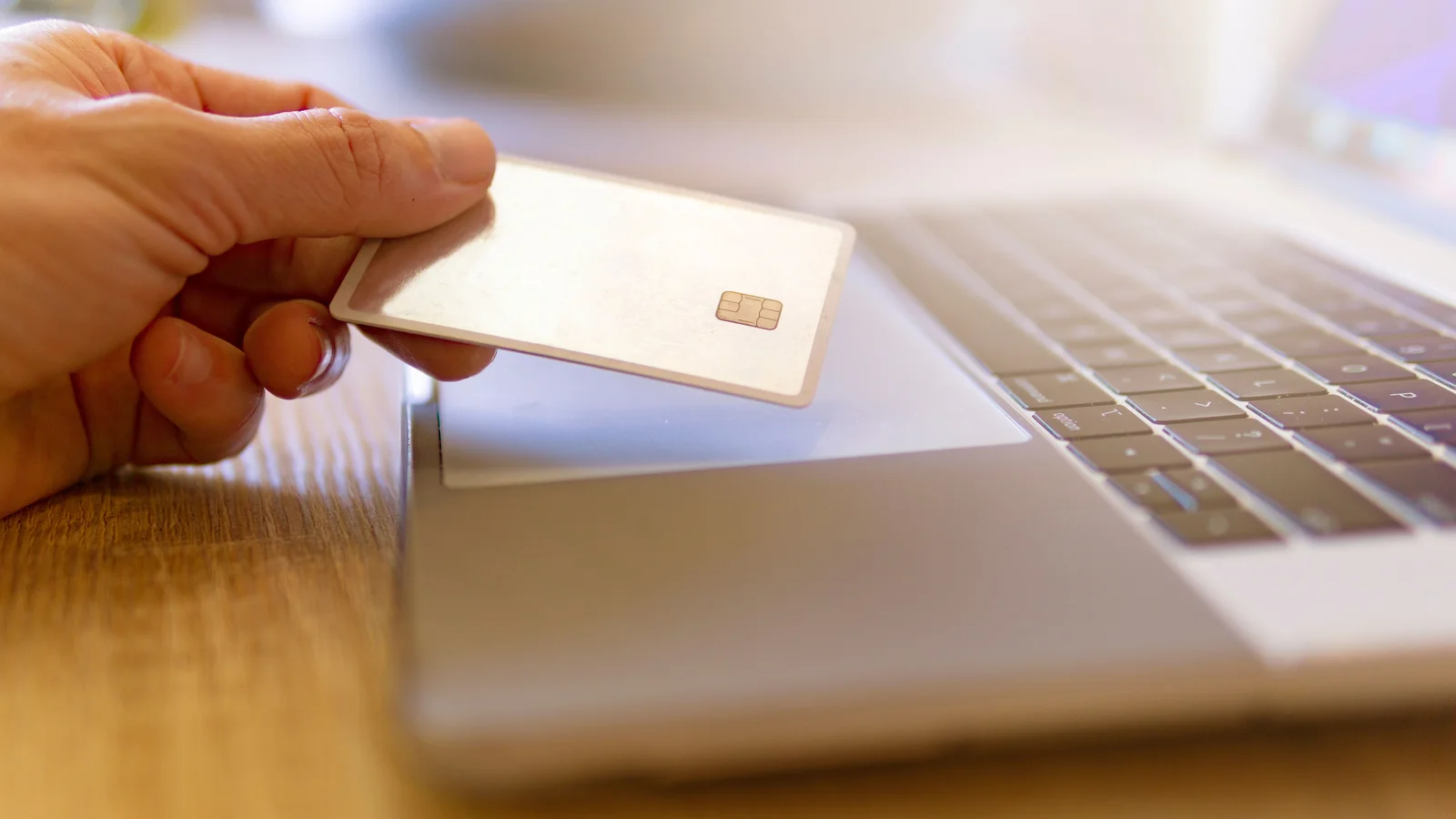 Une main tient une carte blanche à puce devant le clavier d’un ordinateur portable.