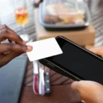Une personne présente une carte blanche devant une tablette au comptoir d’un restaurant.