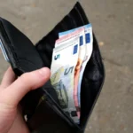Une main tient un portefeuille noir contenant des billets en euros.