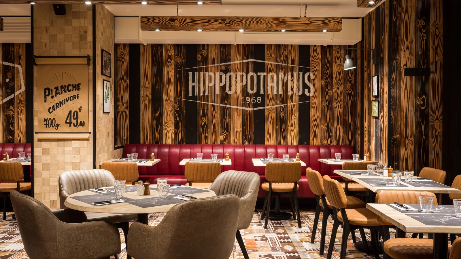 Salle du restaurant Hippopotamus Paris Montparnasse, avec banquettes rouges, fauteuils et décor en bois.