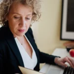 Une femme travaille sur un ordinateur portable, un carnet ouvert devant elle.
