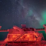 Le laboratoire IceCube éclairé en rouge au pôle Sud, sous la Voie lactée et une aurore australe.