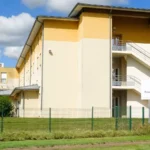 Façade jaune et beige de l’Ehpad des Charmes, avec un escalier extérieur et le panneau de la résidence.