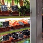 Légumes et étiquettes de prix dans un magasin à Paris, avec une balance suspendue.