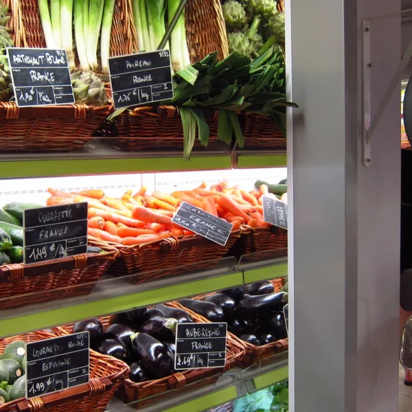 Légumes et étiquettes de prix dans un magasin à Paris, avec une balance suspendue.