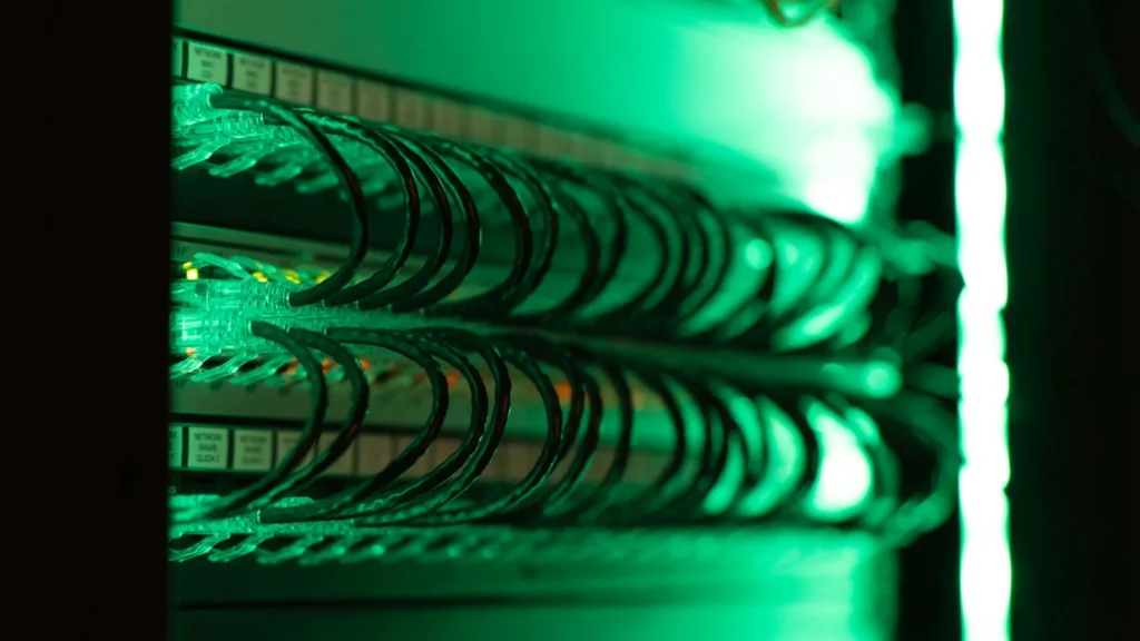 Câbles réseau raccordés à une baie informatique sous un éclairage vert.