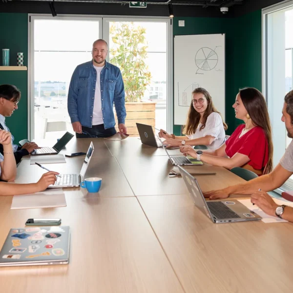 Six personnes réunies autour d’une table avec des ordinateurs portables dans un espace de coworking.
