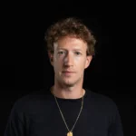 Mark Zuckerberg, dirigeant de Meta, en pull sombre devant un fond noir.