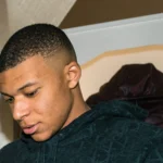 Portrait de Kylian Mbappé portant une veste sombre.