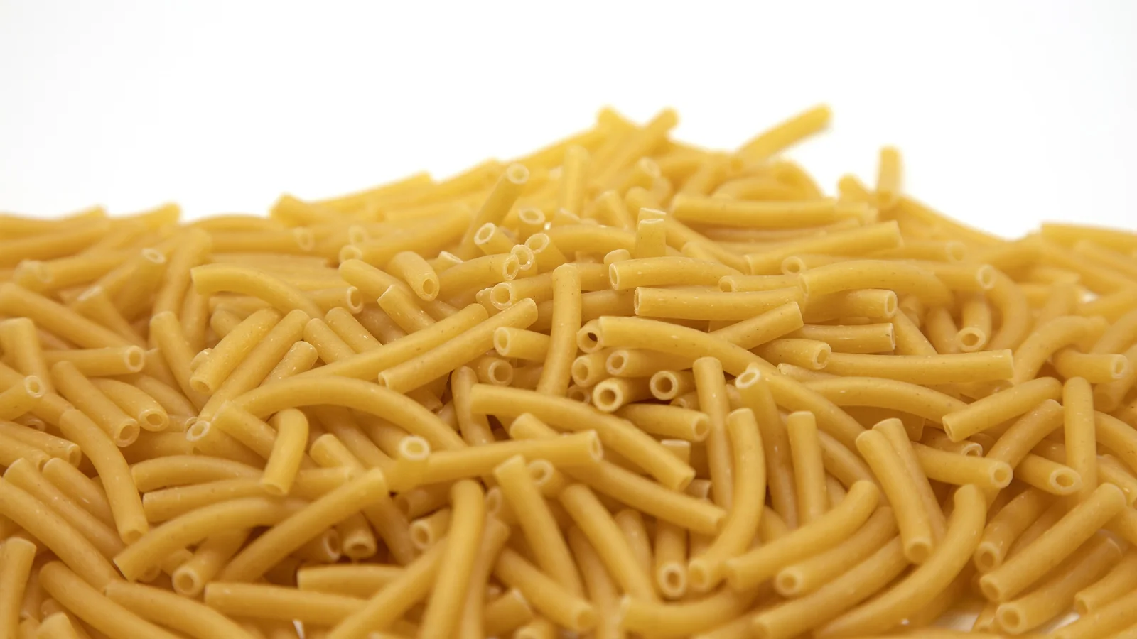 Un tas de macaronis secs jaunes sur fond blanc.