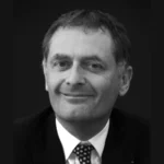 Portrait en noir et blanc de Philippe Juvin, en costume et cravate, sur fond sombre.