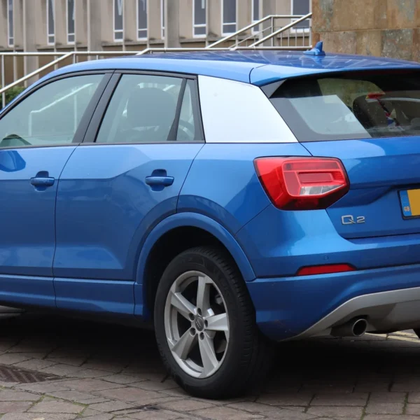 Audi Q2 bleu vu de trois quarts arrière, avec son habillage de pilier C visible.