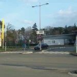 Entrée de l’usine Renault du Mans, avec ses bâtiments, son portail et des drapeaux jaunes.