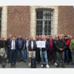 Groupe de personnes devant un bâtiment en briques, avec des drapeaux Klégé et des pancartes de soutien.