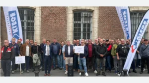 Groupe de personnes devant un bâtiment en briques, avec des drapeaux Klégé et des pancartes de soutien.