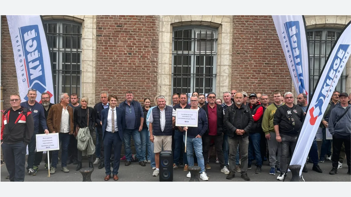 Groupe de personnes devant un bâtiment en briques, avec des drapeaux Klégé et des pancartes de soutien.