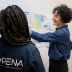 Deux personnes échangent devant des plans au mur, l’une portant une veste avec le logo SAPRENA.