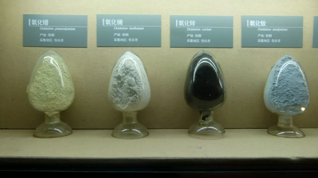 Échantillons d’oxydes de terres rares dans quatre récipients en verre, présentés sous leurs étiquettes.