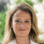 Portrait d’Olivia Grégoire, en veste sombre et chemise blanche, devant un jardin.
