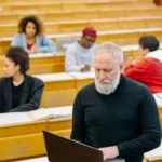 Un homme debout utilise un ordinateur portable dans une salle de cours, devant plusieurs participants.
