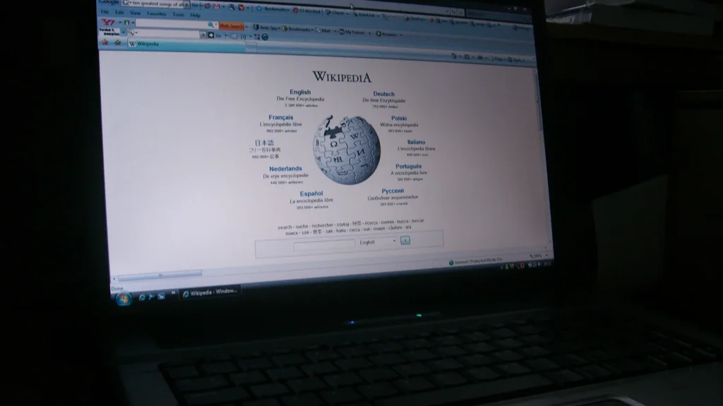 Page d’accueil de Wikipédia affichée sur un ordinateur portable posé devant des livres.